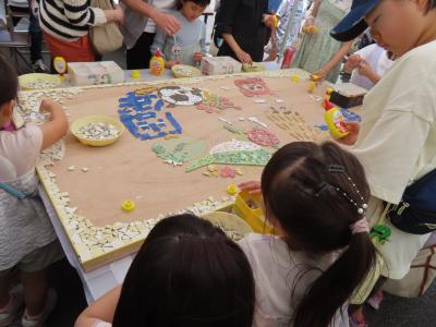 細かいタイルを敷き詰めて、市制施行70周年記念のロゴを完成させることを目指す子どもたちの写真