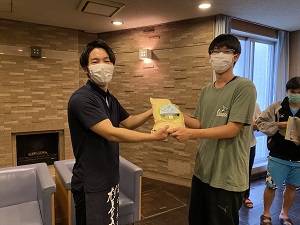 電気通信大学国際交流会館で商品を渡している写真です